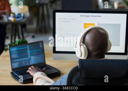 Focus on bald head of young male programmer in headphones typing on laptop keypad while decoding data by workplace Stock Photo