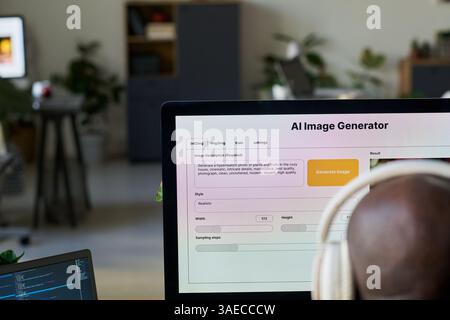 Image generator on screen of desktop computer standing in front of young African American male designer in headphones Stock Photo