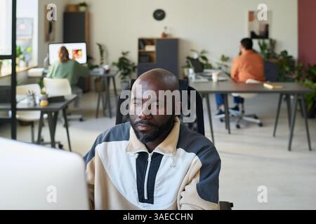 Young serious African American programmer sitting by workplace in front of desktop computer and looking at screen Stock Photo