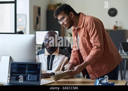 Two serious male programmers looking through new software product on screen of desktop computer during presentation Stock Photo