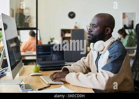 Young serious man concentrating on work over new content while looking at screen of desktop computer with AI image generator Stock Photo