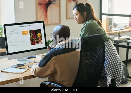 Two programmers looking at screen of desktop computer while using AI image generator and creating new content by workplace Stock Photo