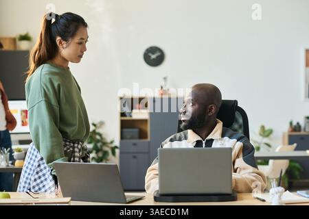 Young serious male employee looking at female colleague during discussion of details of developing new software Stock Photo