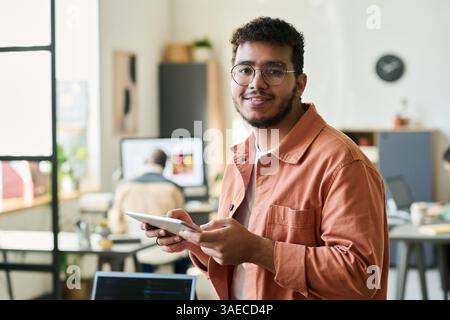 Young smiling male programmer or software developer looking at camera while working over new project in coworking space Stock Photo
