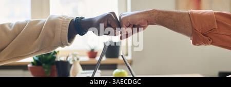 Header of punch bump of two young intercultural male programmers over laptops during work over new software in office Stock Photo