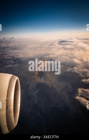 Airplane engine intake flying over a cloudy background with a wildfire in the background. Stock Photo