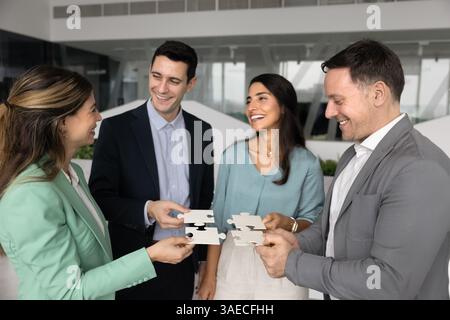 Team of happy stakeholders joining pieces of puzzle in office Stock Photo
