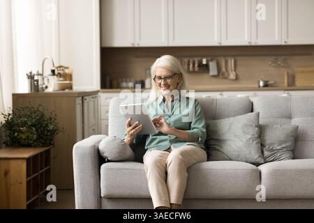 Happy middle aged female pensioner using digital pad at home Stock Photo