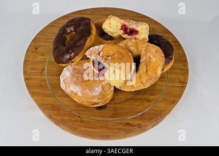 A delicious assortment of donuts, including chocolate glazed and jelly-filled, presented on a rustic wooden tray for a delightful treat on a white Stock Photo