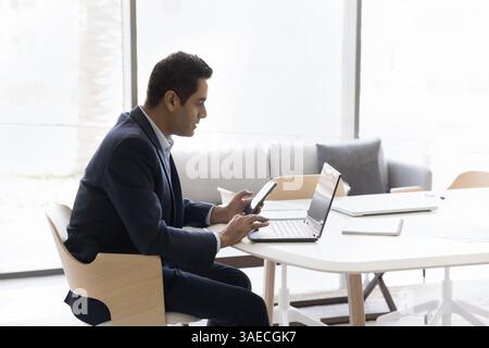 Workflow of mature Indian businessman using laptop and smartphone Stock Photo