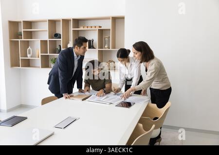 Four corporate members review documents, making notes, strategizing in boardroom Stock Photo