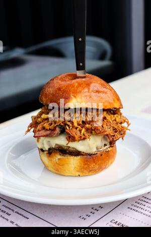 smashed burger, pulled pork burger on brioche bun and a knife on a white plate. Restaurant set up Stock Photo