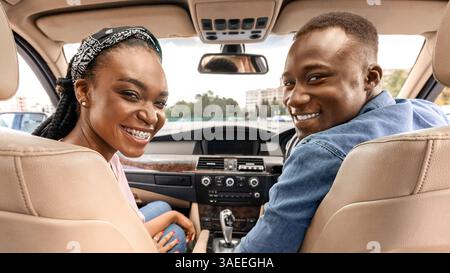 Happy afro american couple posing in auto, looking at backseat Stock Photo