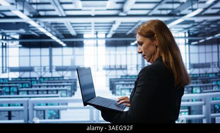 Computer scientist doing yearly maintenance using laptop to prolong data center equipment life span. IT specialist in server hub facility monitoring server infrastructure using device, camera B Stock Photo