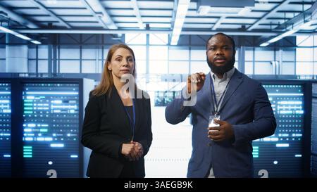 Teamworking technicians in high tech data center workspace looking at hologram visualization. Programmer and colleague working on securing server room hardware using AR tech, camera B Stock Photo