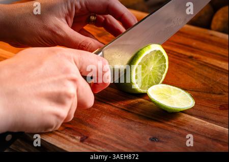 Person slicing a lime on wood cutting board Stock Photo