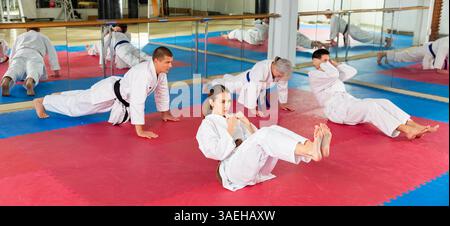 Men and women in kimono doing crunches and push-ups in gym Stock Photo
