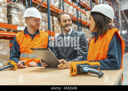 Manager holding a clipboard, engaging in discussion with warehouse workers about improving inventory control and enhancing operational efficiency Stock Photo
