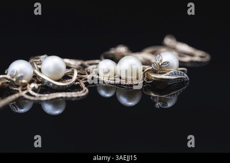 Gold earrings and rings with white pearls lie on a black mirror surface Stock Photo