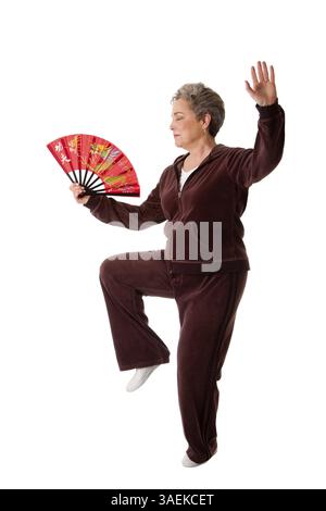 Beautiful Senior woman doing Tai Chi exercise with red dragon fan to keep her joints flexible, isolated, New York, USA, North America Stock Photo