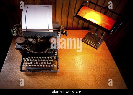 Wooden desk lit up by an old lamp with yellow light and a historic rusty typewriter with a plastified sheet of white paper, Cape May, USA, North Ameri Stock Photo
