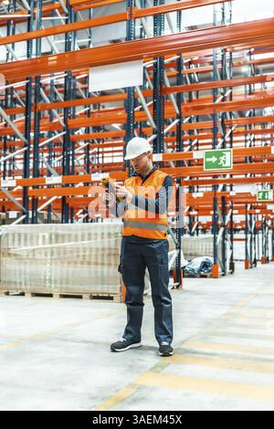 Warehouse worker wearing safety vest and hardhat using barcode scanner to track packages in modern logistics center Stock Photo