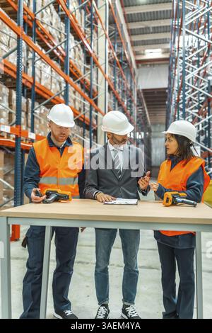 Warehouse workers and manager discussing logistics while using barcode scanners in a large distribution center Stock Photo