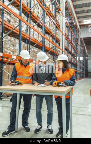 Warehouse workers and manager meeting, discussing logistics and inventory using barcode scanner and clipboard in a large distribution center Stock Photo