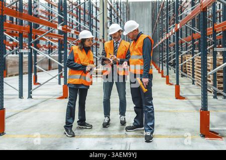 Warehouse workers and a manager in safety vests collaborating on inventory management with barcode scanners and clipboards Stock Photo