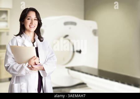 Beautiful happy female doctor physician radiologist holding patient medical chart and pen standing in CT CAT Scan room at hospital, isolated, New York Stock Photo