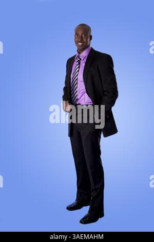 Handsome happy African American corporate business man smiling, wearing black suit with purple shirt, standing with authority with hand in pocket, iso Stock Photo