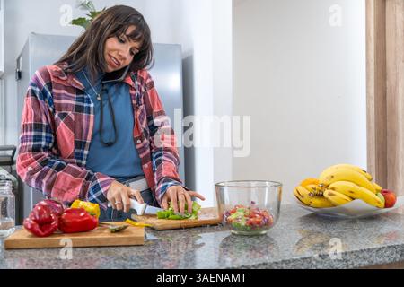 Young woman preparing healthy meal and talking on cellphone in modern kitchen Stock Photo