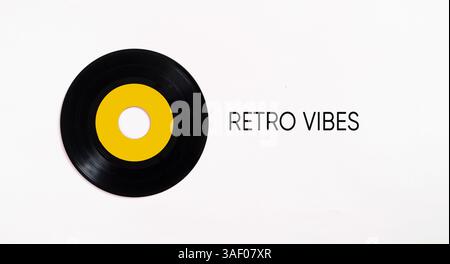 Black vinyl record with yellow label on white background with text retro vibes, bringing back the nostalgic atmosphere of past decades Stock Photo