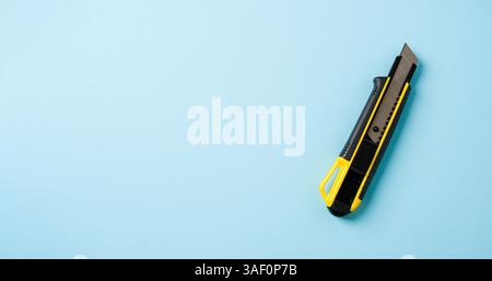 Top view of yellow and black utility knife on blue background Stock Photo