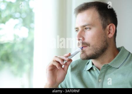 Handsome man vaping looking through a window at home Stock Photo