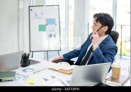 Businessman or male office worker is thinking thoughtfully while holding at pen to his temples. thinking thoughtfully while sitting in the office. Stock Photo
