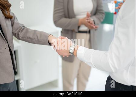 Two businesspeople or office workers are standing and shaking a hand with their client or partner. Corporate handshake. Sealing the deal or contract. Stock Photo