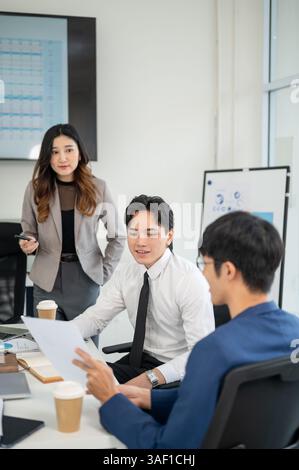 Male office worker is smiling while showing or explaining a document to his coworkers. Businessman and businesswoman is having a meeting in office. Stock Photo
