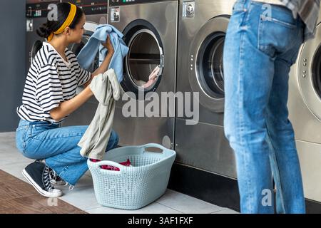 Woman and man using a self-service washing machine in public laundromat washing dirty laundry for hygiene Stock Photo