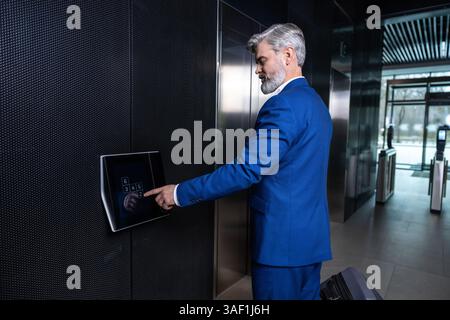 In the business center. Gray-haired elegant businessman pressing the button to call the elevator Stock Photo
