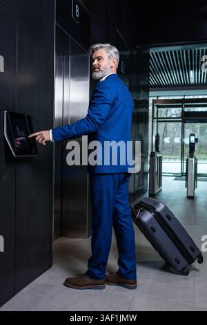 In the business center. Gray-haired elegant businessman pressing the button to call the elevator Stock Photo