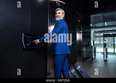In the business center. Gray-haired elegant businessman pressing the button to call the elevator Stock Photo