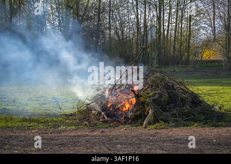 Large heap from branches, twigs and tree cuttings burning on a meadow, garden fire or traditional Easter fire, copy space, selected focus Stock Photo