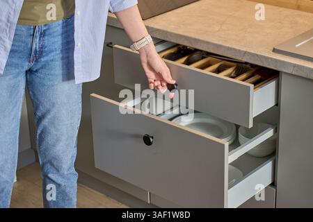 Person opens a kitchen drawer with various utensils in wooden cutlery tray. Woman opening kitchen cabinet. Concept of home organization and functionality interior Stock Photo
