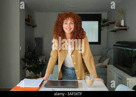 Young businesswoman smiling and posing leaning on her desk at home Stock Photo