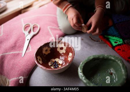 Child threading a needle while crafting on a pink textile surface Stock Photo