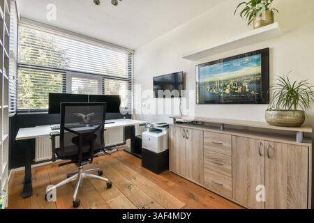 A sleek home office featuring a stylish desk, multiple monitors, wooden flooring, and contemporary decor, creating a productive environment. Stock Photo