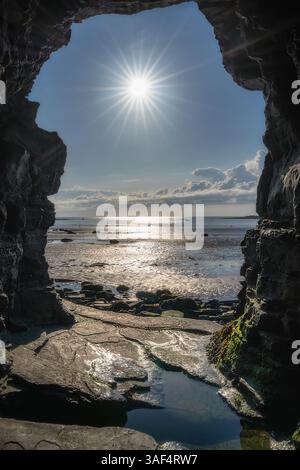The breathtaking view through a magnificent rock arch perfectly showcases the sparkling ocean waters beneath, with sunlight beautifully reflecting on Stock Photo