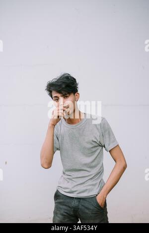 Young asian man in grey shirt posing against a white wall. Expressive pose. Contemporary look. Stock Photo