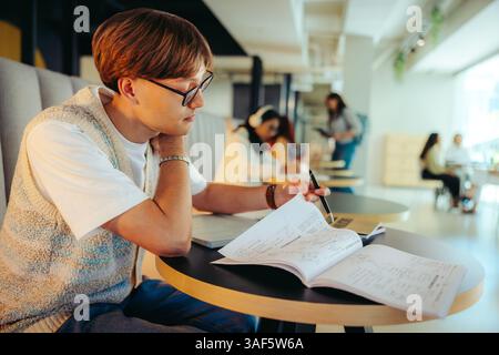 A male high school student is studying intently at a library, surrounded by peers in a collaborative learning environment. Stock Photo